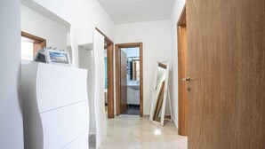 Un couloir étroit avec un réfrigérateur blanc, une porte en bois et un miroir appuyé contre le mur.