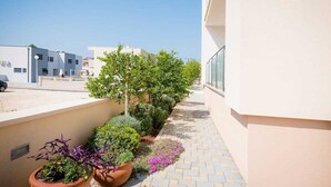 Un étroit couloir extérieur agrémenté de plantes en pot, avec un ciel dégagé.
