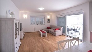 Un salon spacieux comprenant un canapé, une table basse et une table à manger avec des chaises. Une porte-fenêtre coulissante donne accès à un espace extérieur aménagé avec une table et des chaises.