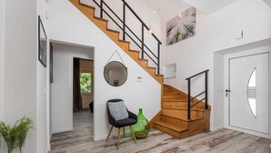 Un interior moderno con una escalera de madera, un espejo redondo, un jarrón verde y una silla negra.