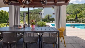 Un área de comedor al aire libre con mesa y sillas, una piscina y vistas del paisaje circundante.