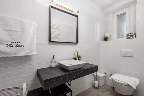 Un baño moderno con un lavamanos blanco, encimera de mármol negro y un espejo sobre el lavamanos.