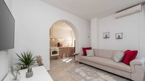 A modern living room with a beige sofa, a coffee table, and a rug. There is a kitchen visible through an archway in the background. - Villa Marcela | Adriatic Luxury Villas (Pridraga)