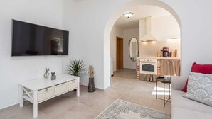 A modern living room with a flat-screen TV, a white console table, and a sofa. There is a kitchen visible through an archway with a stove and cabinets. - Villa Marcela | Adriatic Luxury Villas (Pridraga)