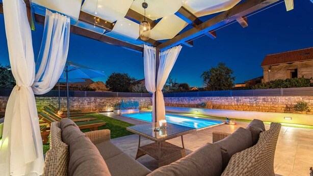 An outdoor patio with a pool, wicker furniture, and draped white curtains. - Villa Marcela | Adriatic Luxury Villas (Pridraga)