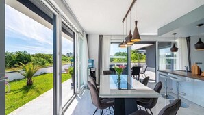 Un espace de salle à manger moderne avec une table en verre, des chaises noires et des luminaires suspendus.