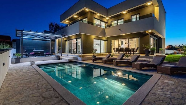 Une maison moderne à deux étages, dotée d’une piscine et d’un espace extérieur aménagé pour se détendre.