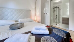 Una habitación de hotel moderna con una cama grande, una mesita de noche, una lámpara de noche, cabina de ducha de vidrio y un armario.