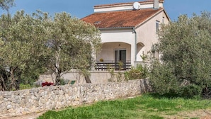 A two-story house with a stone wall in front, a tiled roof, and a satellite dish.