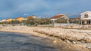 A coastal residential area with houses, a rocky shoreline, and a clear sky.