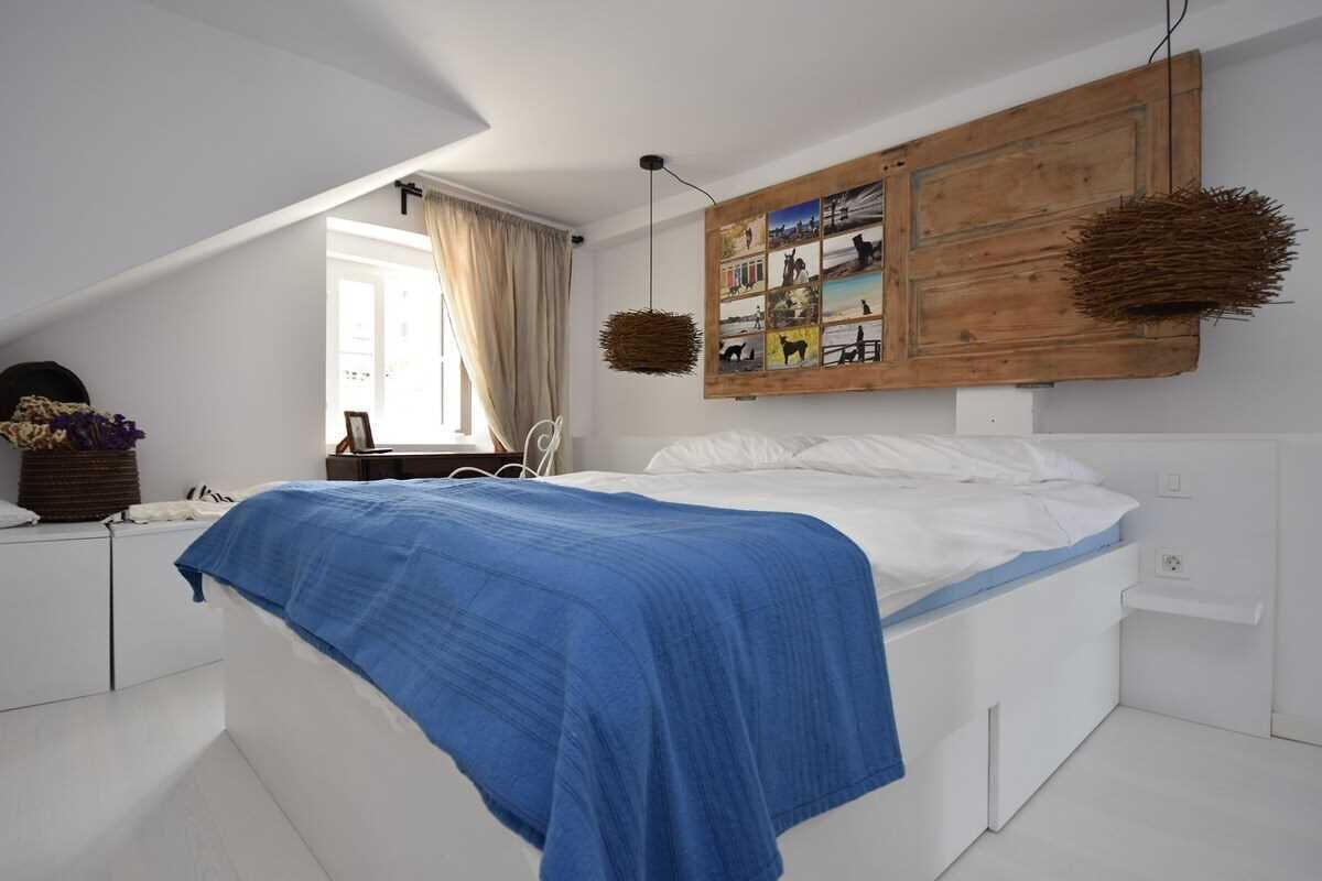 A bedroom with a bed, a wooden headboard, a wall-mounted photo collage, and a hanging basket.