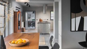 Una cocina moderna con una isla central, un comedor con mesa y sillas de madera, y un cuadro abstracto grande en la pared.