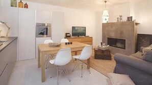 A modern living room with a fireplace, a dining area with a wooden table and white chairs, and a grey sofa. - Artistic Villa B1 - Adriatic Luxury Villas (Radetići)