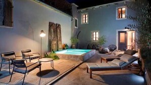 An outdoor pool area with lounge chairs and a table, surrounded by a building with a light blue exterior and a door visible. - Artistic Villa B1 - Adriatic Luxury Villas (Radetići)