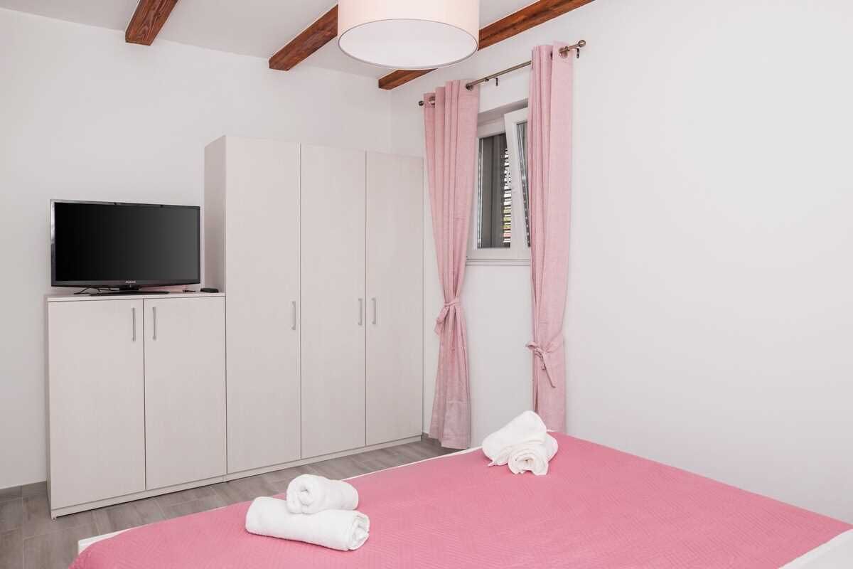 Une chambre à coucher avec un lit, une télévision, une armoire et une fenêtre avec des rideaux.