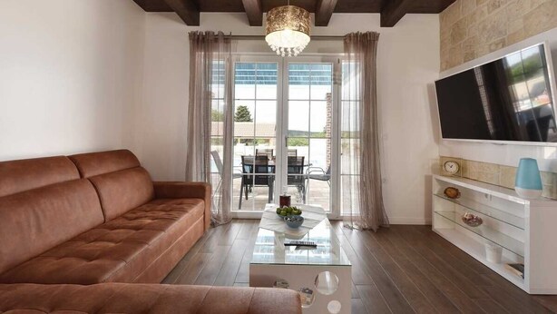 Una sala de estar moderna con un sofá de cuero marrón, una mesa de centro de vidrio y un televisor sobre un soporte blanco.