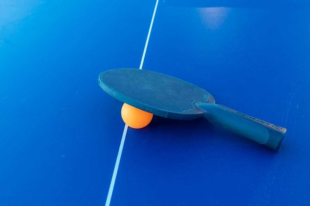 A blue ping pong table with a ball and a paddle.