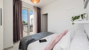 A modern bedroom with a large bed, a tablet on the bed, a ceiling light, and a view of the outdoors through a sliding door. - Villa Pollux | Adriatic Luxury Villas (Vrsi)