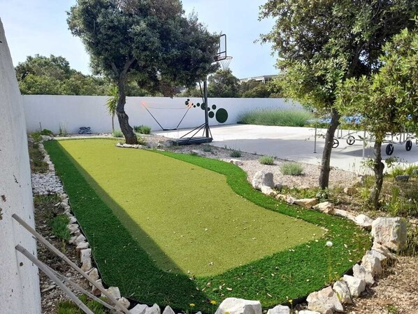 A basketball court with a hoop, surrounded by a well-maintained lawn and a white wall in the background. - Villa Pollux | Adriatic Luxury Villas (Vrsi)