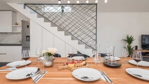 A modern dining area with a wooden table set for a meal, a staircase with a geometric railing, and a minimalist kitchen in the background. - Villa Pollux | Adriatic Luxury Villas (Vrsi)