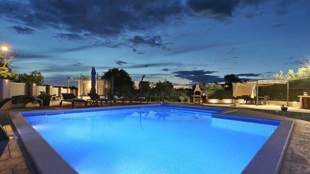 Una piscina con borde de azulejos, rodeada de sillones de descanso y una zona cubierta.