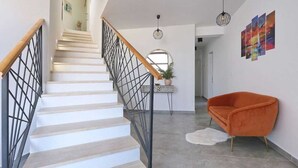 Una escalera con barandilla de madera y balaustres de metal, que conduce a una habitación con una silla moderna color naranja y una alfombra blanca.