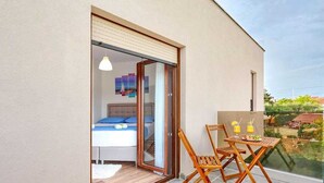Un apartamento moderno con balcón, una cama con ropa de cama azul y una zona de comedor con sillas de madera y una mesa.