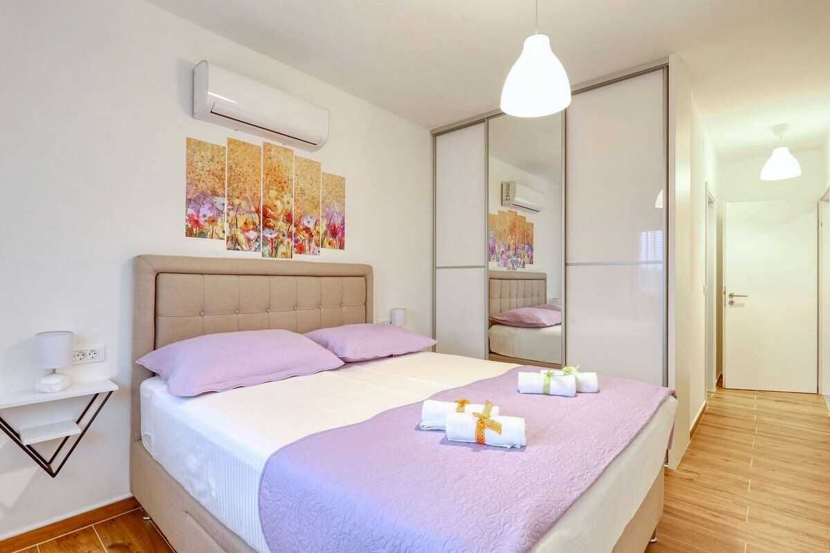 Een moderne slaapkamer met een groot bed, een nachtkastje met een lamp en een wandgemonteerde airconditioning.