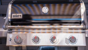 A Weber grill with four burners and a thermometer.