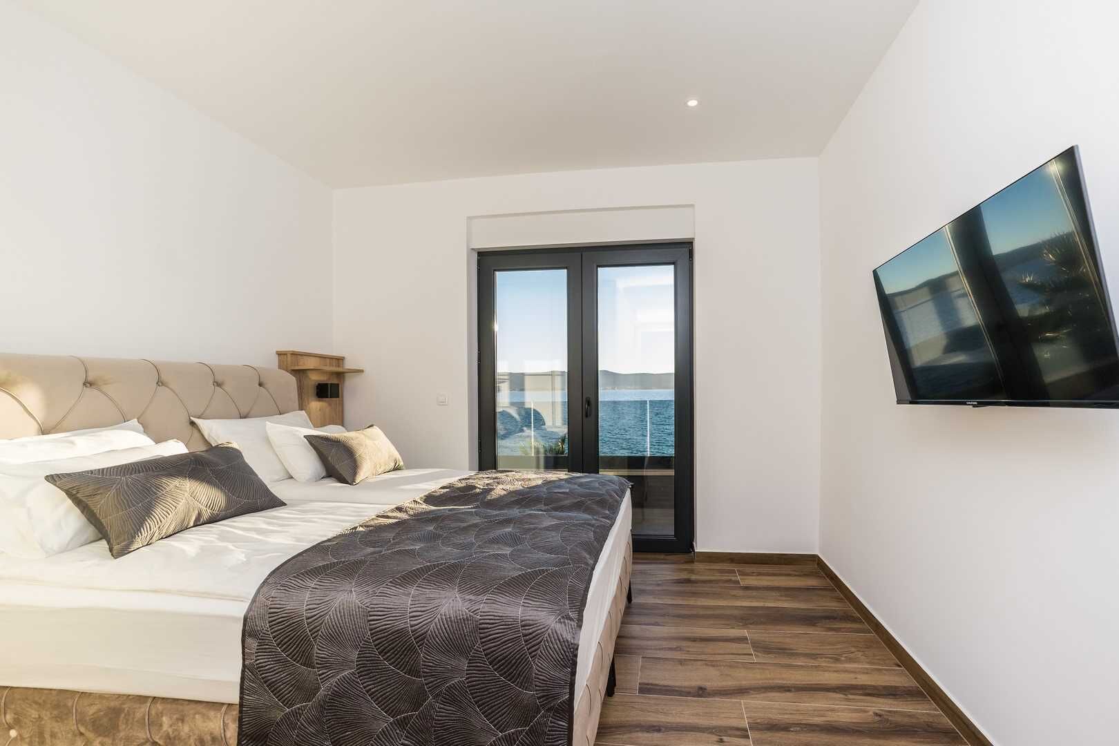 A bedroom with a bed, a television, and a view of the sea through a glass door.