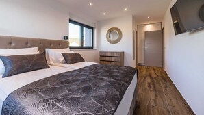 Un dormitorio moderno con una cama grande, un espejo, un televisor y una puerta que da a otra habitación.