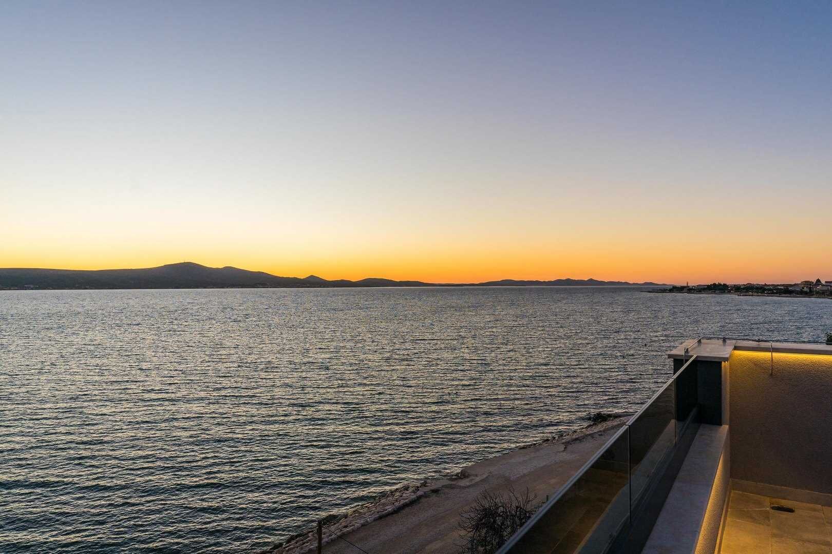 Vistes costaneres sota un cel serè, amb una mar tranquil·la i una cadena de muntanyes a la distància.