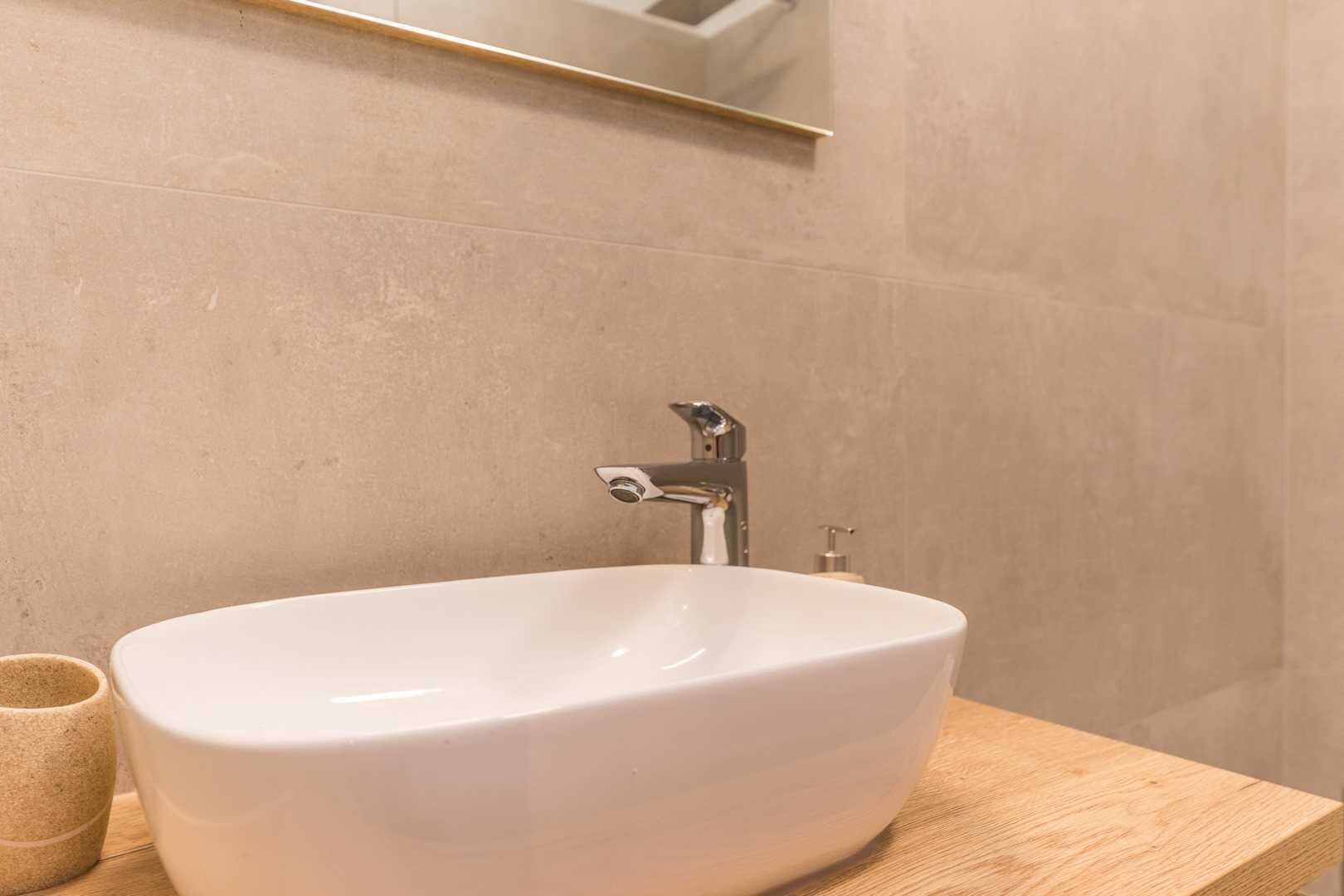 A bathroom with a white sink, a wooden countertop, and a mirror above the sink.