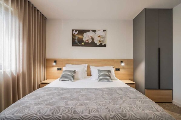 Une chambre d’hôtel avec un grand lit, deux tables de chevet, une tête de lit, une œuvre d’art accrochée au mur et une armoire.