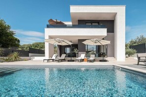 Une maison moderne à deux étages dotée d’une piscine, d’un espace salon extérieur et d’un patio.