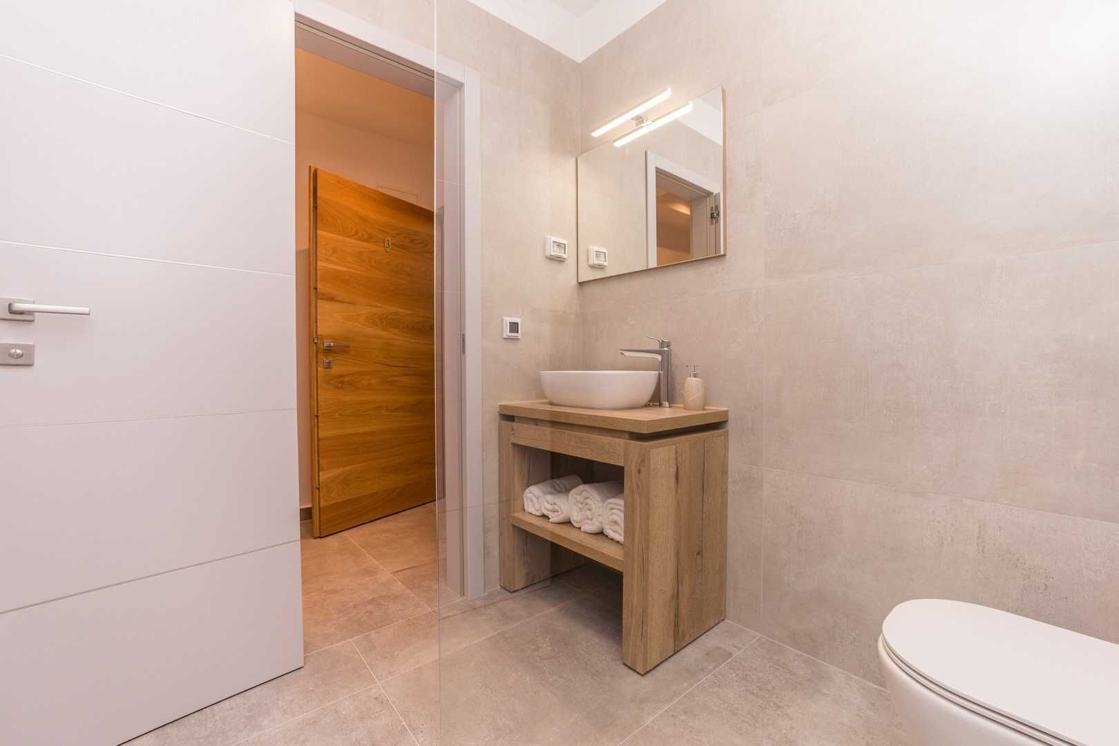 A modern bathroom with a wooden vanity, a large mirror, and a toilet.