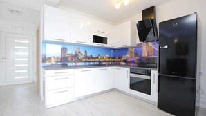 Una cocina moderna con armarios blancos, un refrigerador negro y un mural con vista a la ciudad.