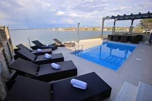 A poolside area with lounge chairs and a pergola overlooking a body of water.