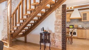 A wooden staircase with stone walls, a small round table with a vase, and a kitchen area with wooden cabinets and a stove.