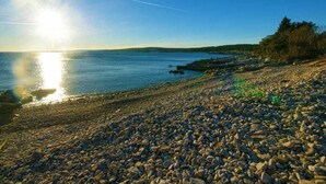 A pebbled beach with a clear sky and calm water reflecting the sun.
