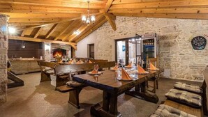 A rustic dining area with wooden beams, stone walls, a fireplace, and a dartboard.
