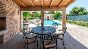 A covered patio with a pool, outdoor seating, and a brick wall.