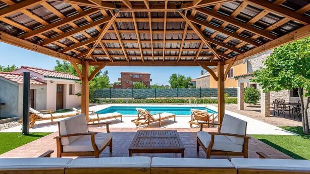 A covered outdoor area with a pool, lounge chairs, and a wooden pergola structure.