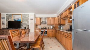 A modern kitchen with wooden cabinets, a stainless steel refrigerator, and a dining area with a wooden table and chairs.