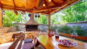 An outdoor dining area with a wooden table, benches, and a brick oven. - Villa Meline | Adriatic Luxury Villas (Donja Hlapa)
