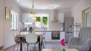 A compact kitchen with white cabinets, a dining area with a table and chairs, and a living area with a sofa and a vase of flowers. - Villa Meline | Adriatic Luxury Villas (Donja Hlapa)