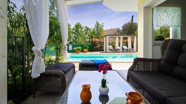 A sunlit patio with wicker furniture, a glass table, and a view of a swimming pool and garden. - Villa Meline | Adriatic Luxury Villas (Donja Hlapa)