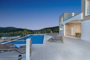 Ein moderner Poolbereich mit Liegestühlen und Essplatz, mit Blick auf eine hügelige Landschaft.