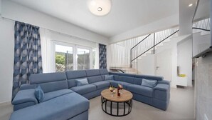 Una sala moderna con un amplio sofá modular en forma de L, una mesa de centro redonda y una escalera que sube a un piso superior.