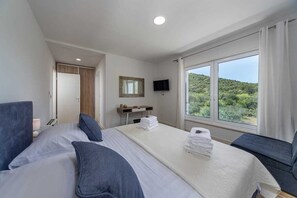 Ein Hotelzimmer mit einem großen Bett, einem Schreibtisch mit Flachbildfernseher und einem Fenster mit Blick ins Grüne.